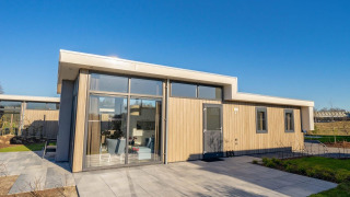 Modern Pavilion lodge with large windows, light wood exterior and stone patio on a sunny clear day