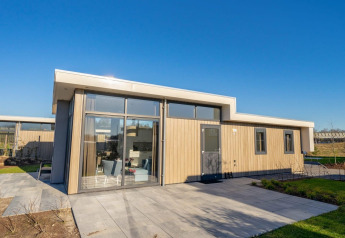 Moderne Pavilion-lodge met grote ramen, lichte houten gevel en ruim terras onder een helderblauwe lucht