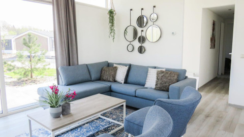 Moderne woonkamer in Pavilion at Zuiderzee, Nederland, met blauwe zetel, ronde spiegels en grote ramen.