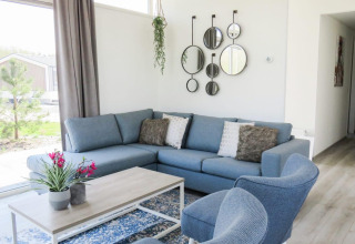 Moderne woonkamer in Pavilion at Zuiderzee, Nederland, met blauwe zetel, ronde spiegels en grote ramen.