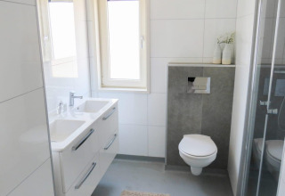 Moderne badkamer in Pavilion at Zuiderzee lodge in Nederland met dubbele wastafel, zwevend toilet en douche.