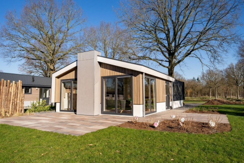 Moderne lodge met grote ramen bij Pavilion aan de Zuiderzee in Nederland, omgeven door bomen en gazon.