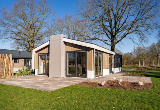 Moderne lodge met grote ramen bij Pavilion aan de Zuiderzee in Nederland, omgeven door bomen en gazon.