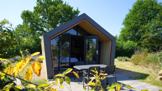 Lodge Solo Retreat 2 moderne avec grande façade vitrée, terrasse agréable et jardin verdoyant sous le soleil.