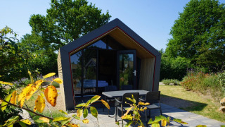 Modern Solo Retreat 2 lodge with large glass front, cozy terrace, and lush garden under blue sky.