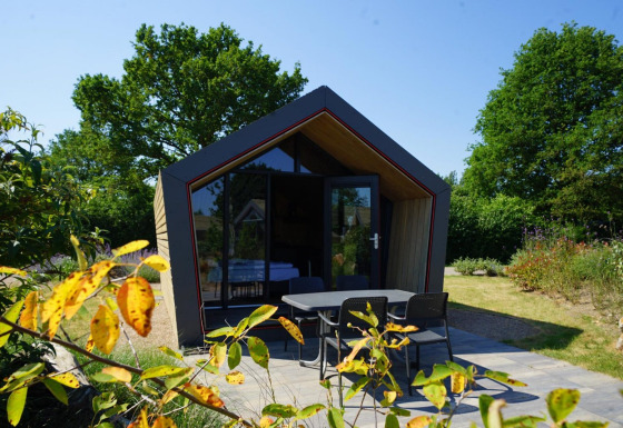 Moderne Solo Retreat 2-lodge met grote glazen gevel, knusse terras en groene tuin onder blauwe lucht.