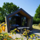 Moderne Solo Retreat 2-lodge med stor glasfacade, hyggelig terrasse og grønne omgivelser i sommersolen.