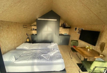 Binnenzicht van Solo Retreat 2 lodge in Zuiderzee, Nederland, met bed, tv, tafeltje en kitchenette.