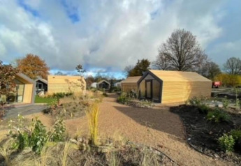 Zicht op Solo Retreat 2 lodge bij Zuiderzee in Nederland, met moderne houten huisjes en omringende natuur.