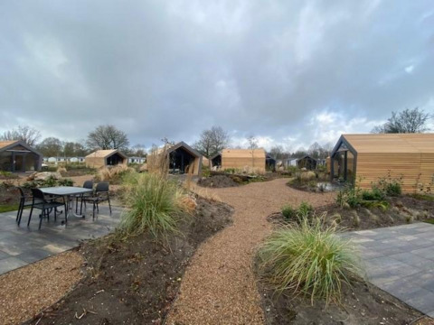 Buitenaanzicht van meerdere Solo Retreat 2-lodges bij Zuiderzee in Nederland, met paden en tuinen.