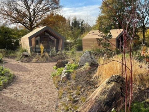 Twee moderne houten lodges bij Solo Retreat 2, Zuiderzee, Nederland, in een natuurlijke tuinomgeving.