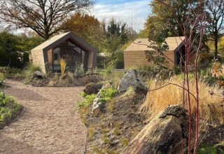 Twee moderne houten lodges bij Solo Retreat 2, Zuiderzee, Nederland, in een natuurlijke tuinomgeving.