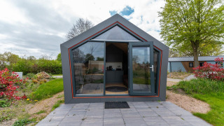 Front exterior view of Solo Retreat 4 lodge with glass doors, tiled patio, and lush greenery around.