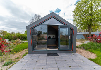 Voorzijde van Solo Retreat 4 lodge met glazen deur, betegeld terras en omgeven door groen.