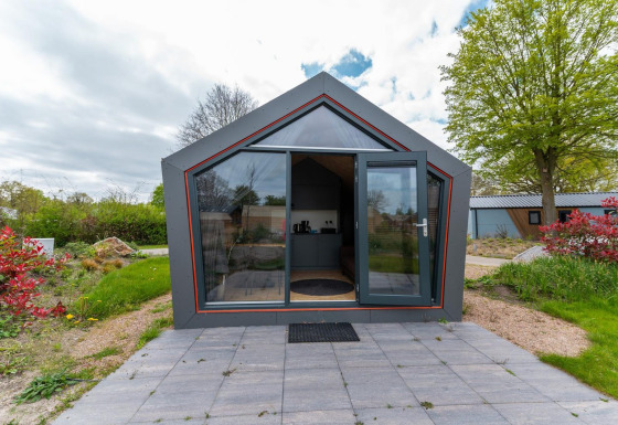 Voorzijde van Solo Retreat 4 lodge met glazen deur, betegeld terras en omgeven door groen.