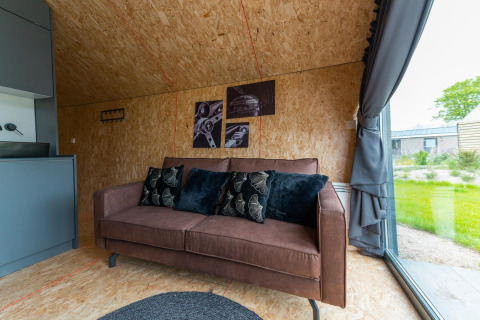 Gemütliches Wohnzimmer in Solo Retreat 4 im Zuiderzee, Niederlande, mit braunem Sofa und Gartenausblick.