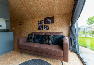 Acogedora sala en Solo Retreat 4 de Zuiderzee, Países Bajos, con sofá marrón y vista al jardín por el ventanal.