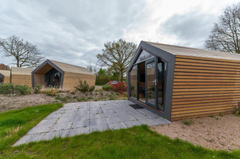 Moderne Holzlodges im Solo Retreat 4 bei Zuiderzee, Niederlande, mit Kies, Grün und bewölktem Himmel.