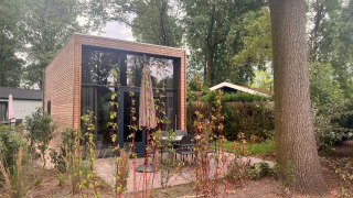 Tiny House 2 moderne avec façade en bois, grandes baies vitrées, terrasse et jardin arboré verdoyant.