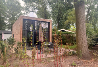 Tiny House 2 moderne avec façade en bois, grandes baies vitrées, terrasse et jardin arboré verdoyant.