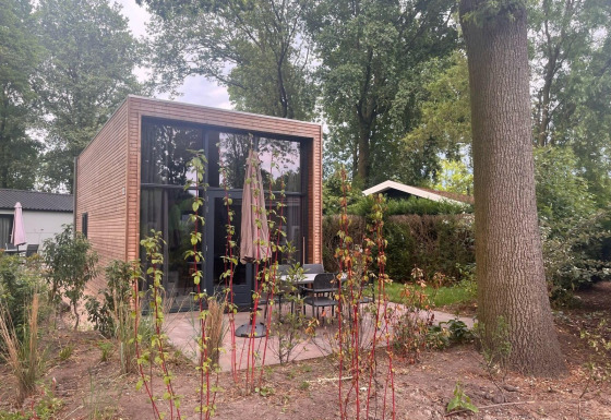Modernes kleines Haus namens Tiny House 2 mit Holzverkleidung, Glasfronten und Terrasse im Grünen.