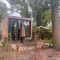 Modern Tiny House 2 met houten gevel, grote glazen ramen en terras midden in groene, bosrijke natuur.