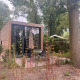 Et moderne, firkantet lille hus kaldet Tiny House 2 med træfacade og stor glasvæg omgivet af natur.