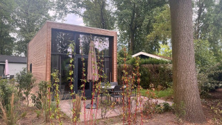 Modernes kleines Haus namens Tiny House 2 mit Holzverkleidung, Glasfronten und Terrasse im Grünen.