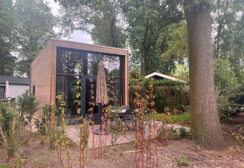Modern Tiny House 2 met houten buitenkant, grote ramen en tuin, gelegen in een bosrijke omgeving.