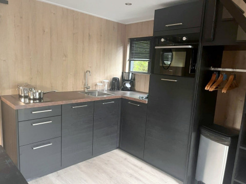 Kompakte moderne Küche in Tiny House 2, Zuiderzee, Niederlande, mit dunklen Schränken und Holzdekor.