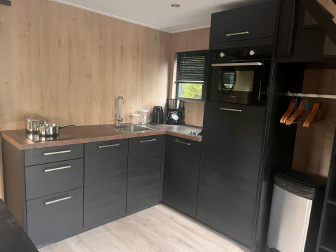 Moderne kitchenette in Tiny House 2 aan Zuiderzee, Nederland, met zwarte kasten en houten muren.