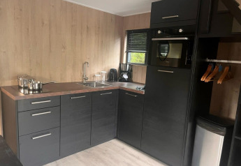 Moderne kitchenette in Tiny House 2 aan Zuiderzee, Nederland, met zwarte kasten en houten muren.