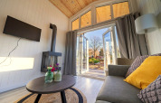 Salon lumineux de Tiny House 4 à Zuiderzee, Pays-Bas, avec canapé, table, poêle et portes ouvertes.