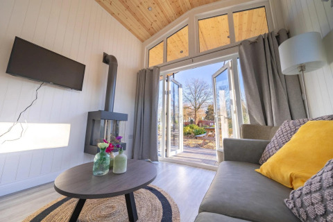 Lichte woonkamer van Tiny House 4 bij Zuiderzee, Nederland, met bank, tafel, haard en open terrasdeuren.
