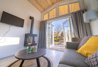 Gezellige living van Tiny House 4 aan Zuiderzee, Nederland, met zetel, tafel, haard en open tuindeuren.