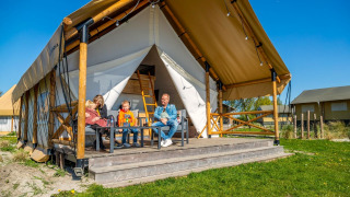 Een gezin ontspant op de veranda van een luxe safaritent genaamd Glampingtent 4 onder een blauwe lucht.