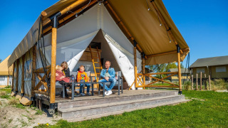 Una familia disfruta en el porche de una tienda de safari de lujo llamada Glampingtent 4 en un día soleado.