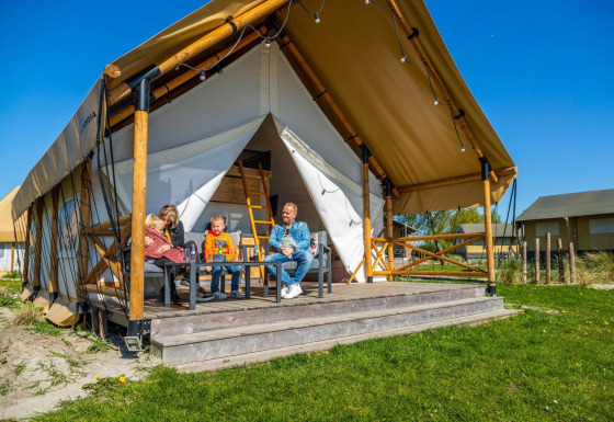 Una familia disfruta en el porche de una tienda de safari de lujo llamada Glampingtent 4 en un día soleado.