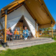 En familie sidder på en terrasse foran en luksuriøs glampingtelt kaldet Glampingtent 4 under en blå himmel.