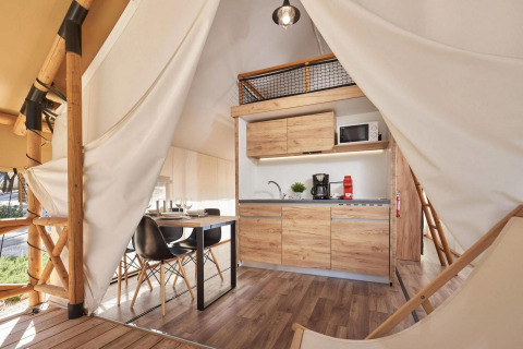 Intérieur de tente glamping moderne avec petite cuisine, table à manger et détails boisés en pleine nature.