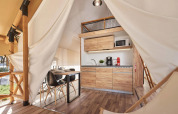 Modern glamping tent interior with small kitchen, dining table, and wood details in a natural setting.