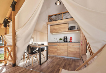 Lyst og moderne glamping-telt med lille køkken, spisebord og træelementer indeni naturskønt område.