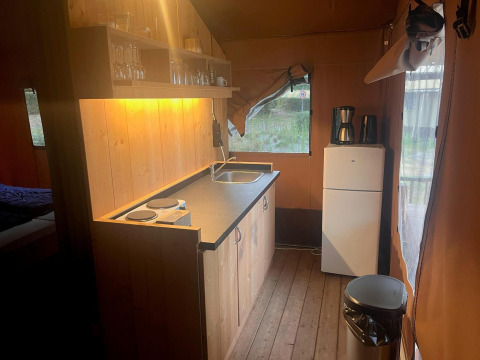 Küchenbereich in einem Glampingtent 4 bei Zuiderzee, Niederlande, mit Herd, Spüle und Kühlschrank.