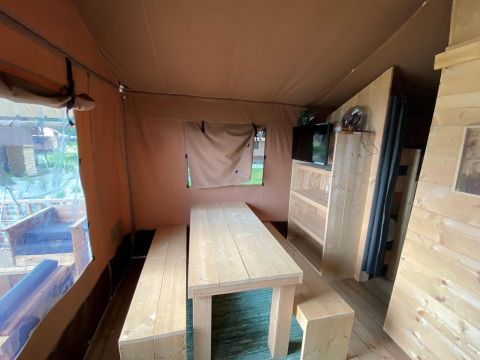 Interieur van een safaritent Glampingtent 4 bij Zuiderzee in Nederland, met houten tafel en banken.