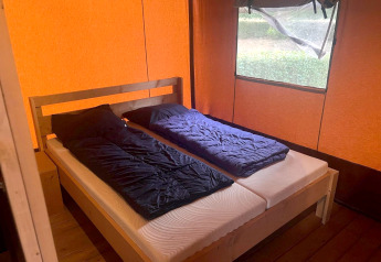 Interieur van safari Glampingtent 4 bij Zuiderzee, Nederland, met twee eenpersoonsbedden en oranje tentwanden.