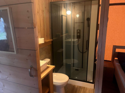 Baño en tienda safari glamping en Zuiderzee, Países Bajos, con ducha, inodoro y lavabo visible.