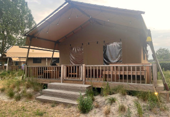 En safari-glampingtelt med træveranda på Zuiderzee i Holland, omgivet af græs og flere telte i baggrunden.