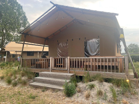 Een safari glampingtent met houten veranda bij Zuiderzee in Nederland, omgeven door gras en natuur.