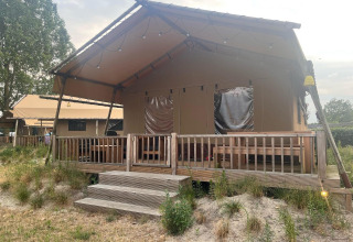 Una tienda de safari glamping con veranda de madera en Zuiderzee, Países Bajos, rodeada de césped y naturaleza.