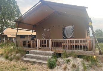 Tenda safari glamping con veranda in legno al Zuiderzee nei Paesi Bassi, circondata da erba e natura.